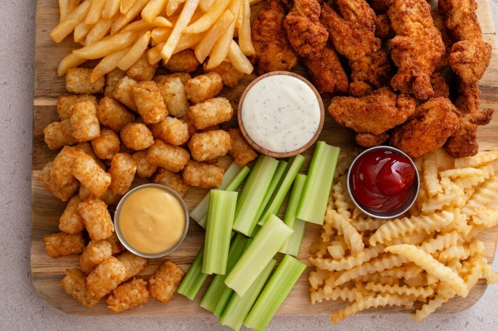 Fried chicken strips and french fries board with sauces and celery